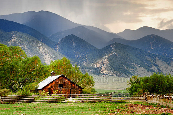 A barn sits at the base of a mountain range, as a rain storm moves in.