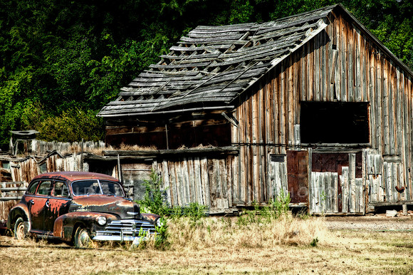 And old rusted car sits beside an old wood barn, creating nostalgia of years long gone.