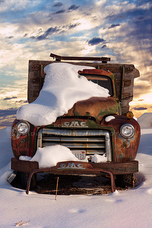 And old GMC truck covered in snow at sunset.